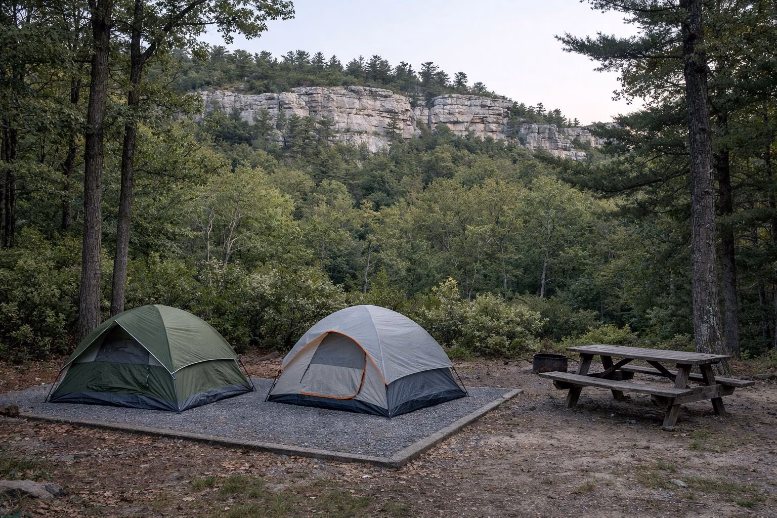 Two dome tents on a gravel tent pad in a wooded campground with a picnic table